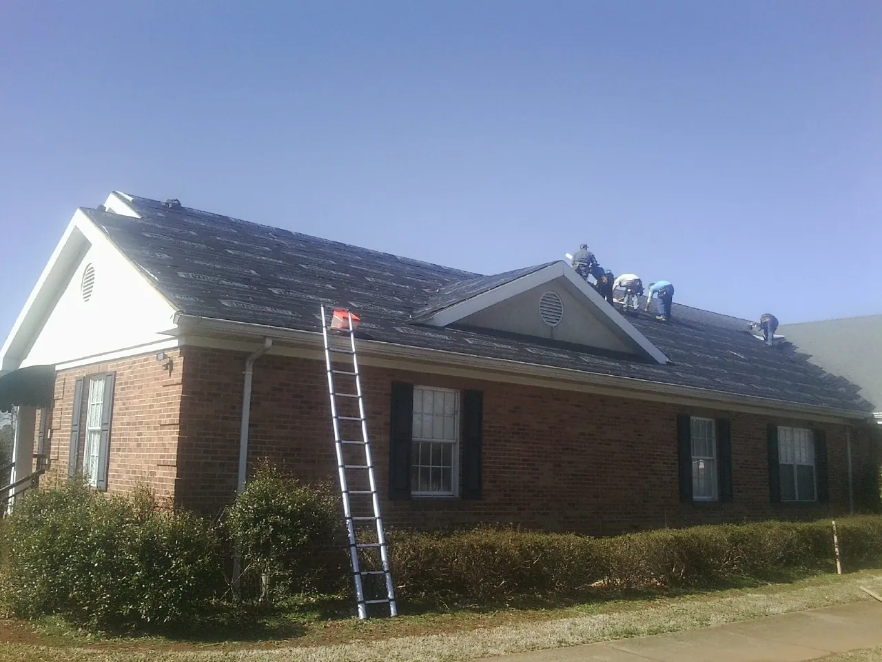 Crew tearing shingles off a brick ranch roof with a ladder set — Emergency Roof Repair work by our crew in Winnetka