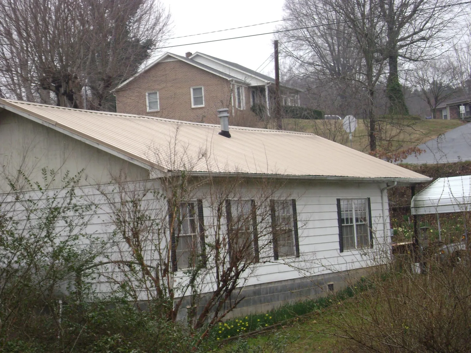Tan metal roof on a white sided house set into a hillside — Commercial Roofing by Roofing Brothers in Winnetka